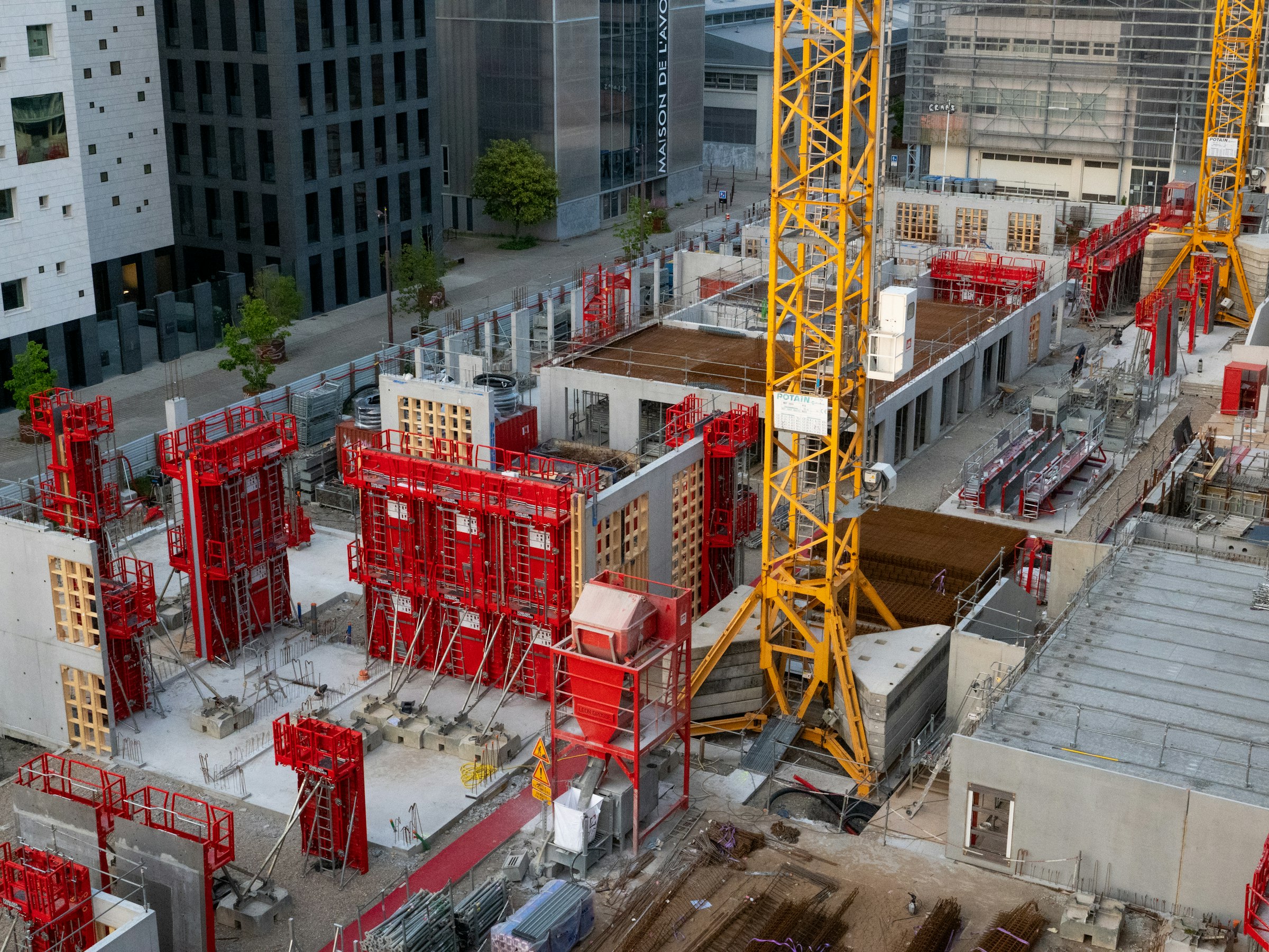 Chantier de gros œuvre vu en plongée : banches, voiles béton et grue à tour entre des immeubles.